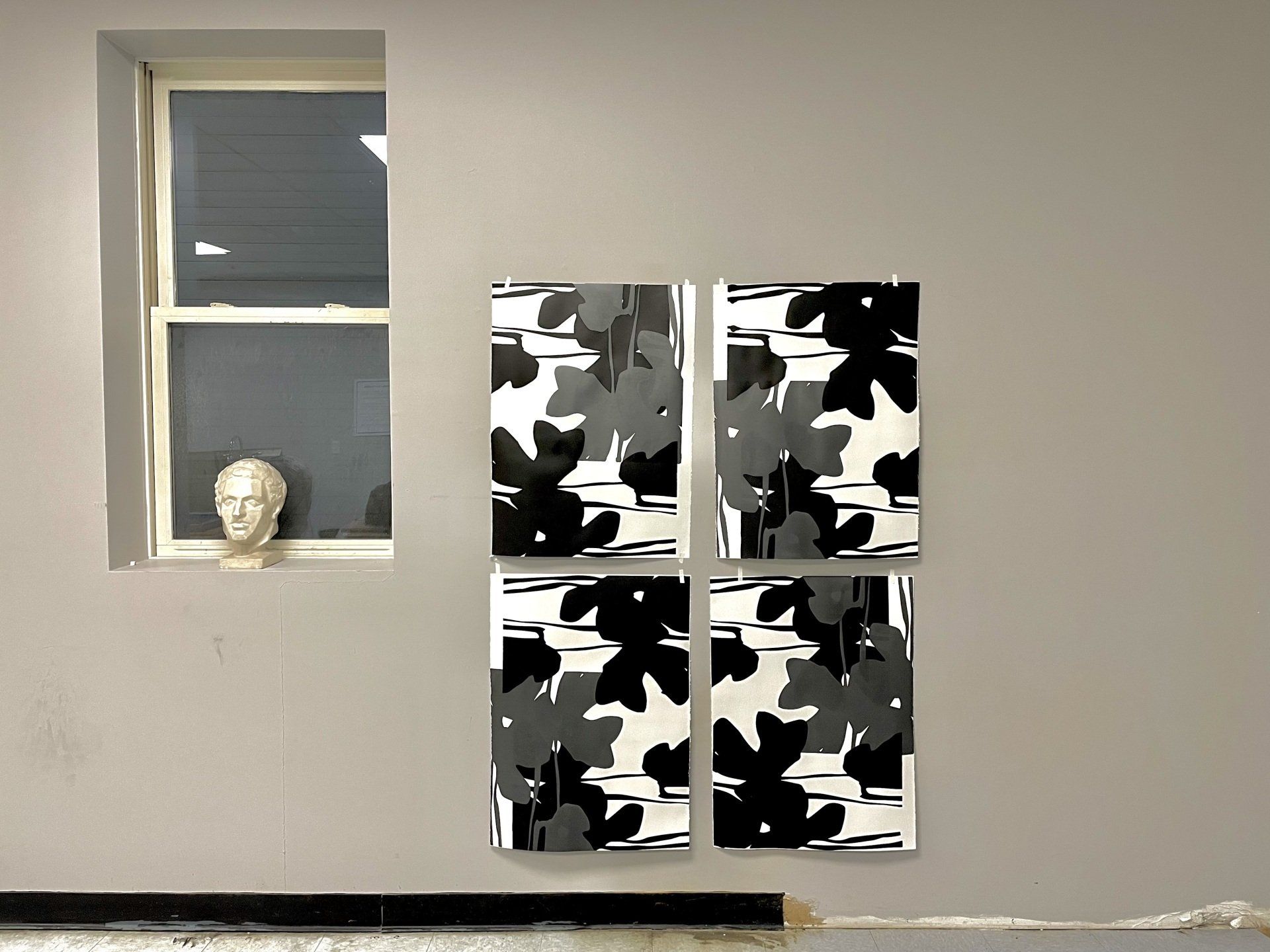 Four black and white paintings are hanging on a wall next to a window