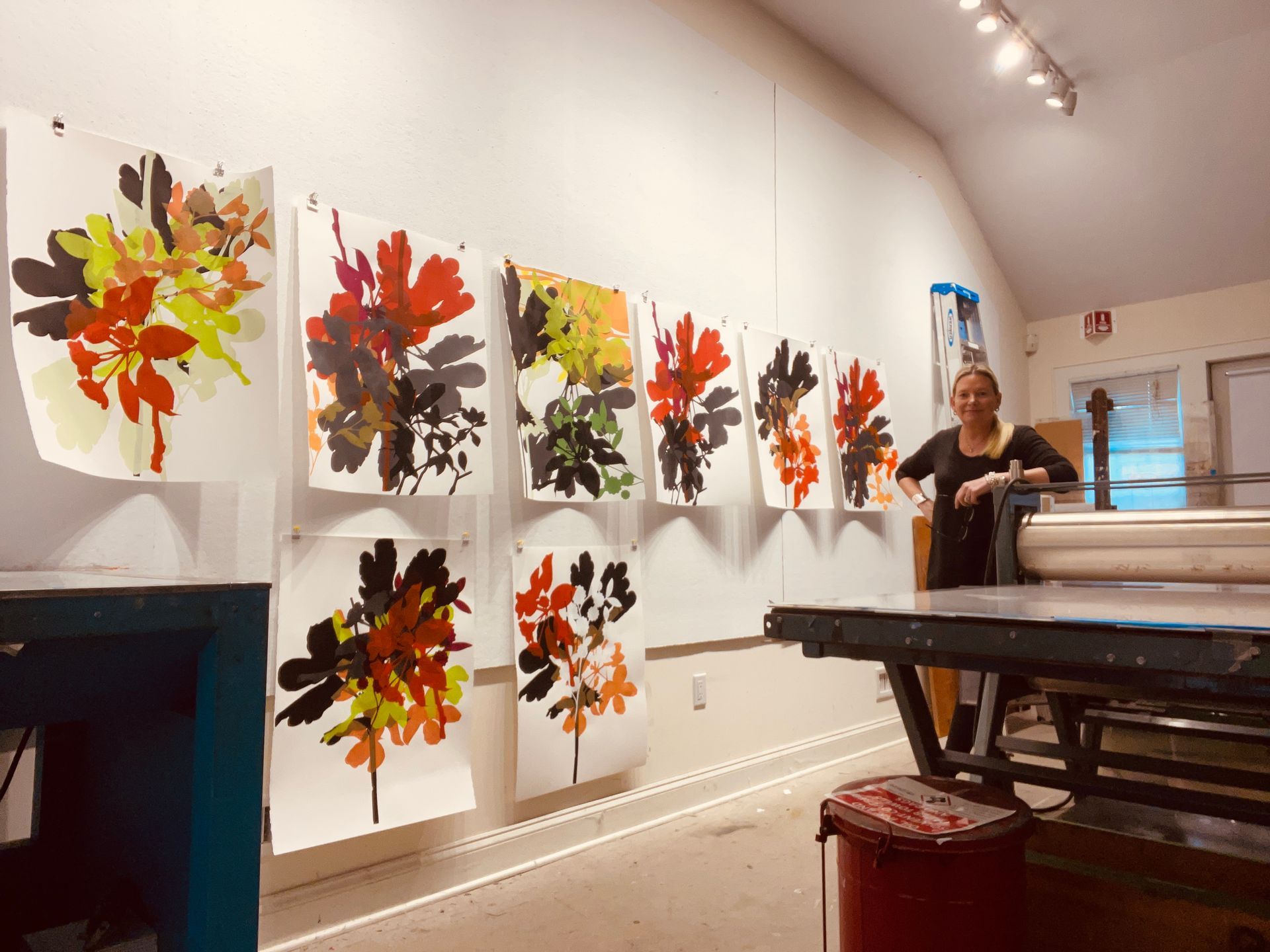 A woman stands in front of a wall with paintings of leaves on it