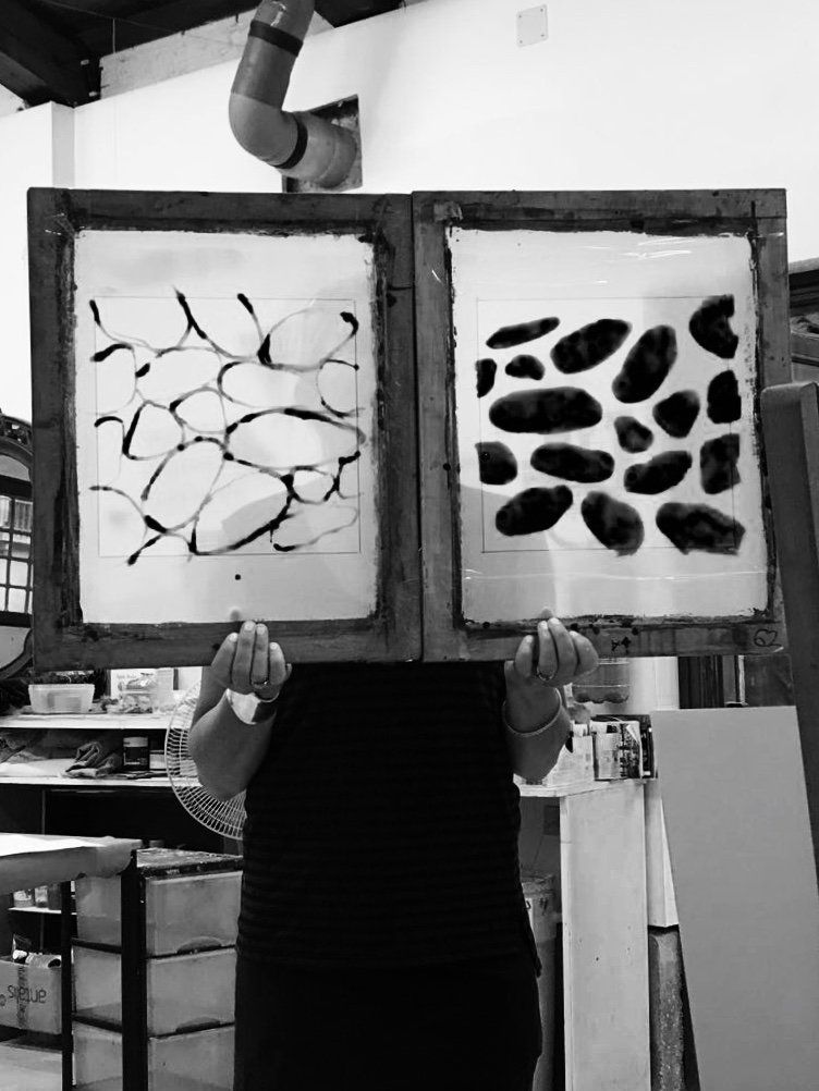 A black and white photo of a person holding two paintings in front of their face.