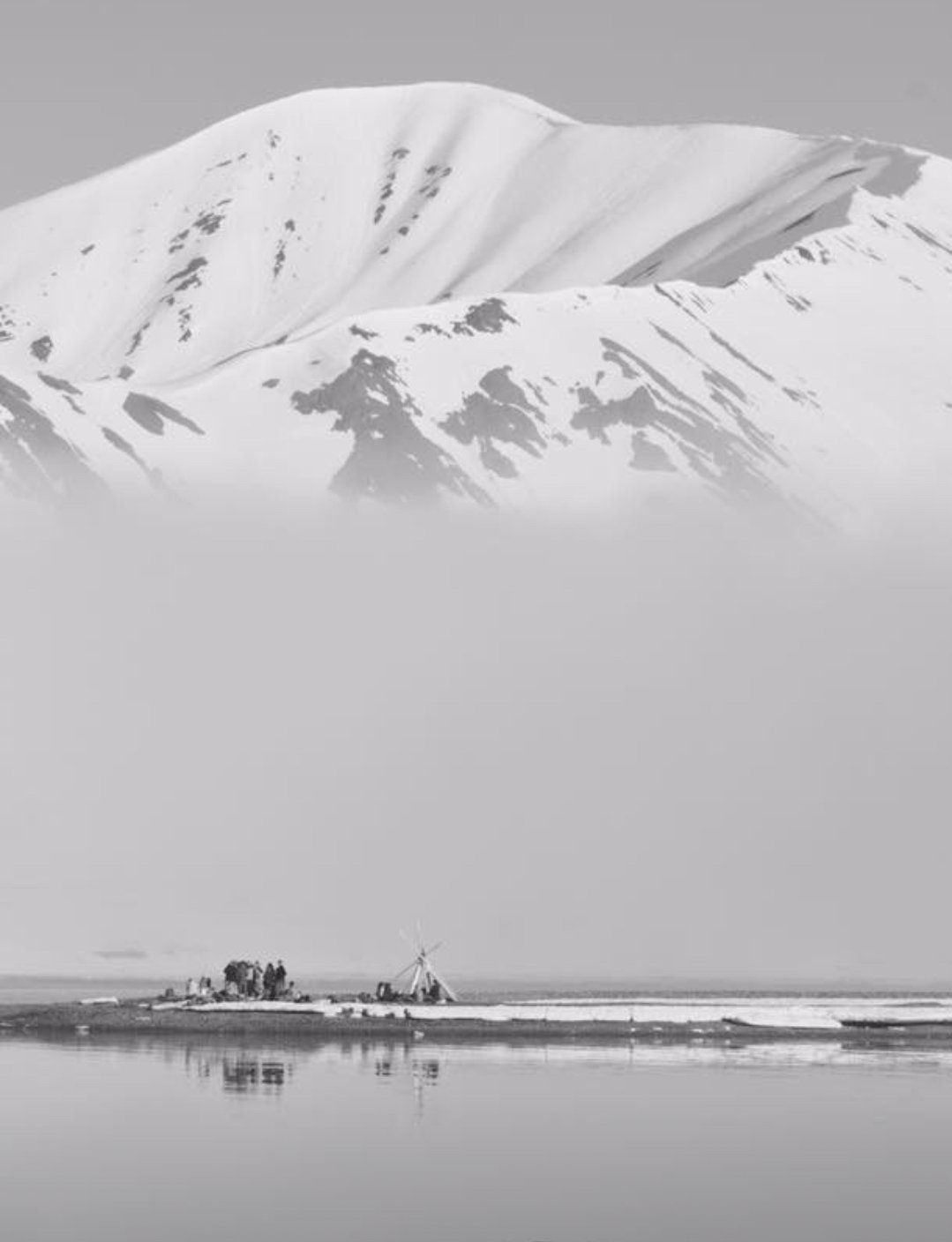 A black and white photo of a snowy mountain and a lake