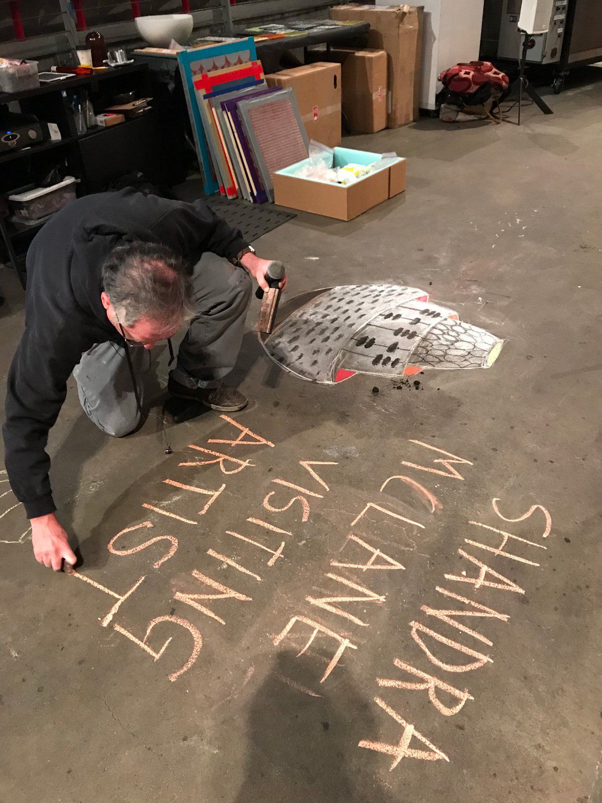 A man is writing on the floor that says sandra mclane visiting artist