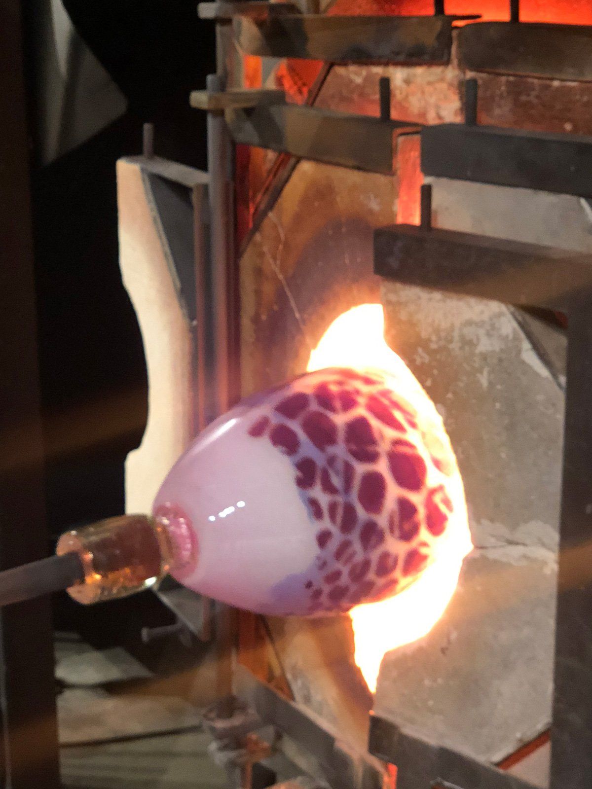 A purple glass object is being blown in a furnace