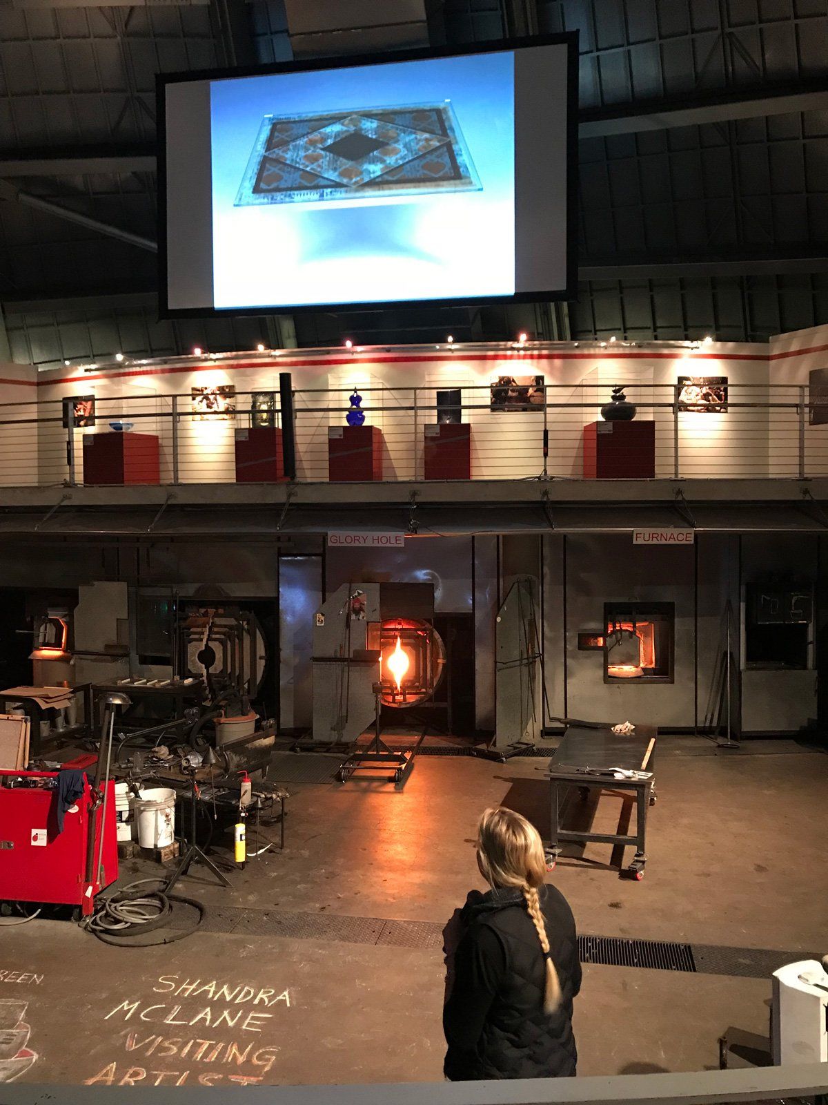 A woman stands in front of a large screen with a picture of a rug on it