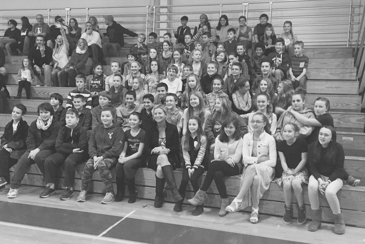 A large group of people are sitting on bleachers in a gym.