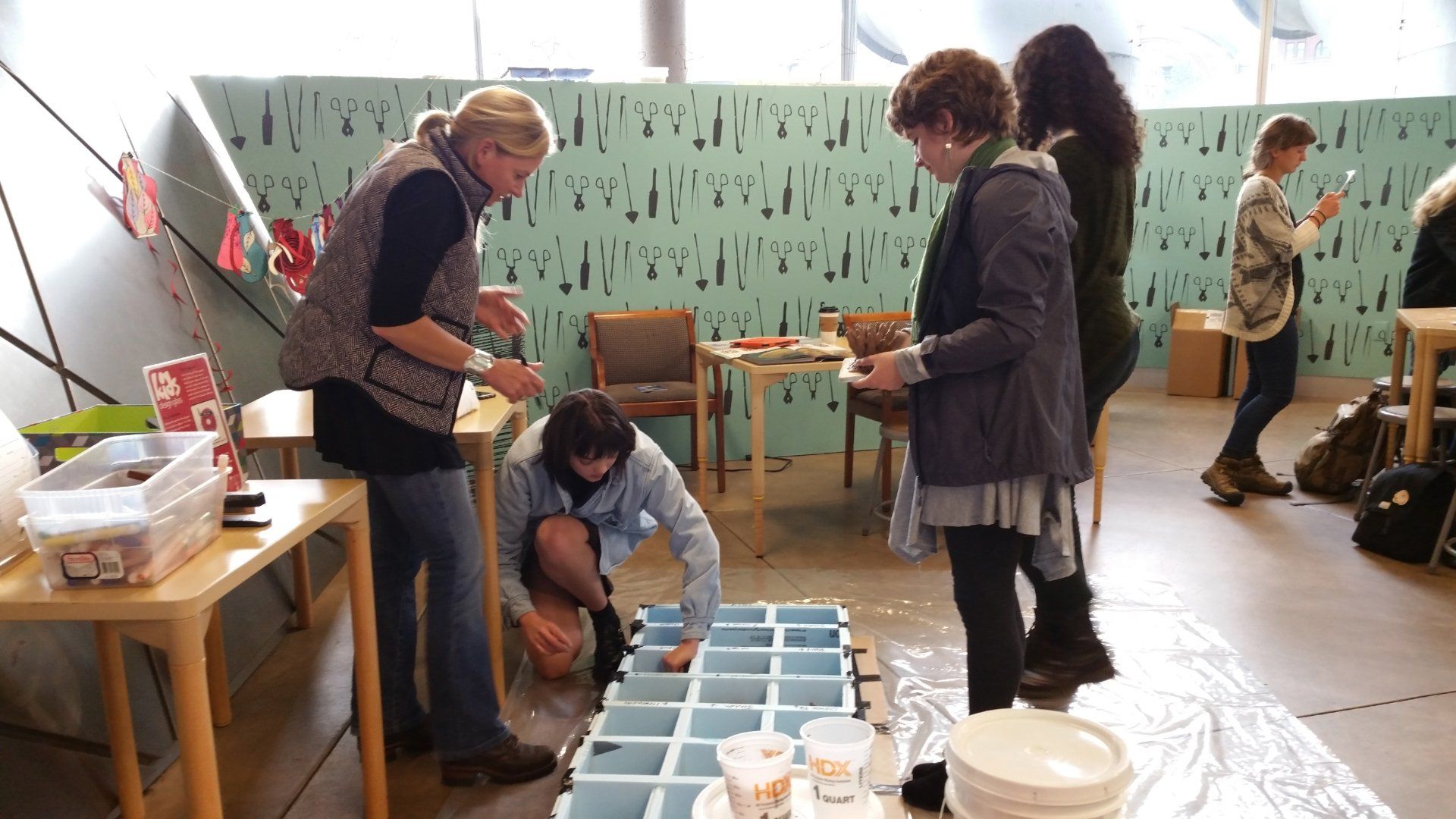 A group of women are working on a table in front of a wall that says ' a ' on it