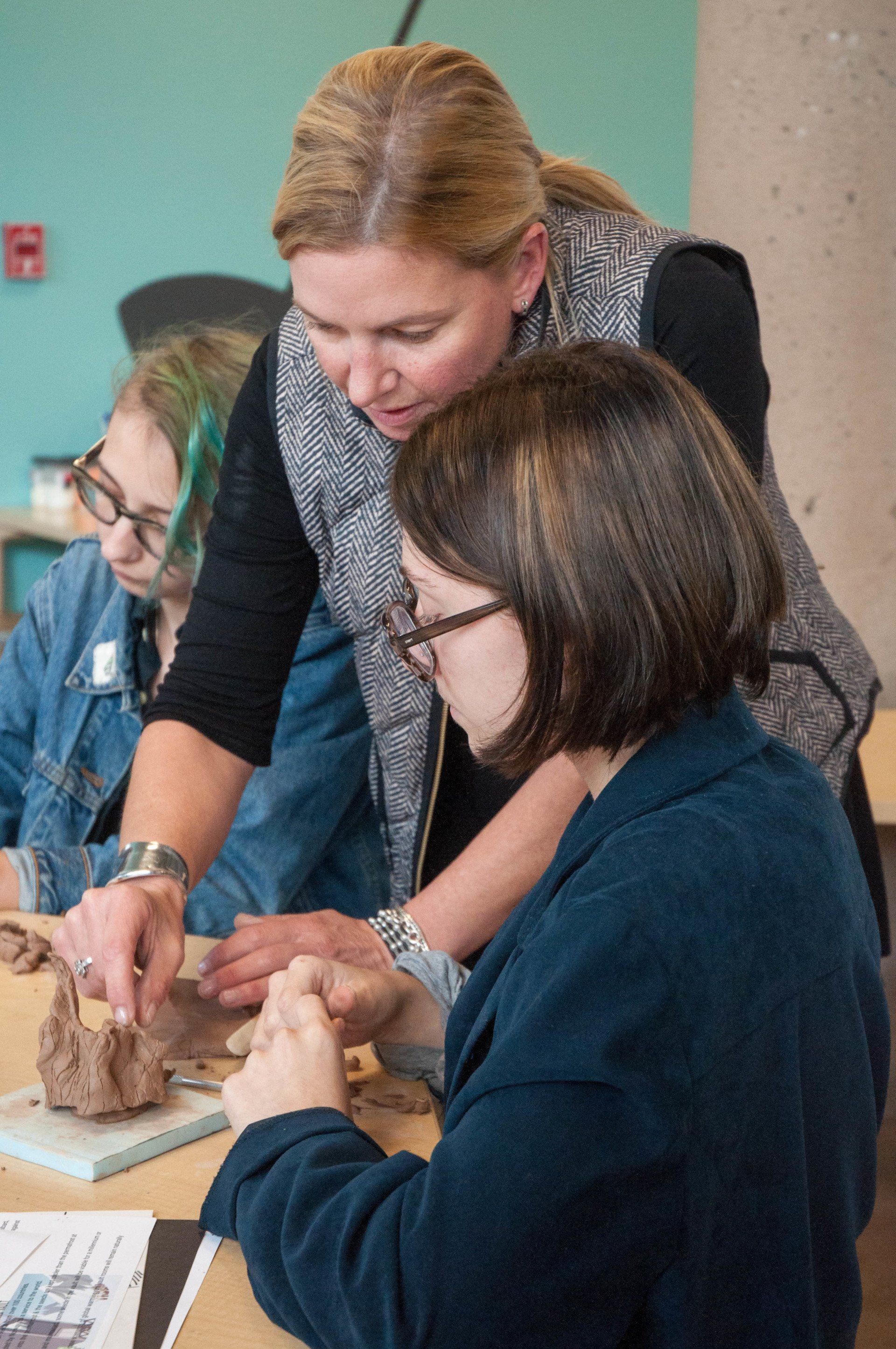 A woman is teaching a young girl how to work with clay
