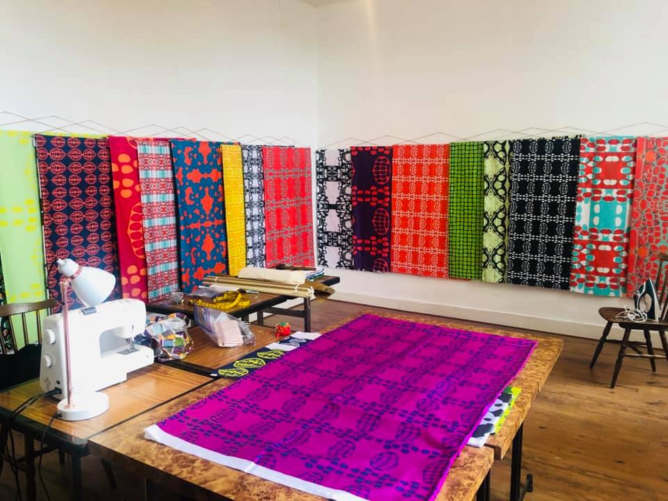 A sewing machine sits on a table in a room filled with colorful fabrics