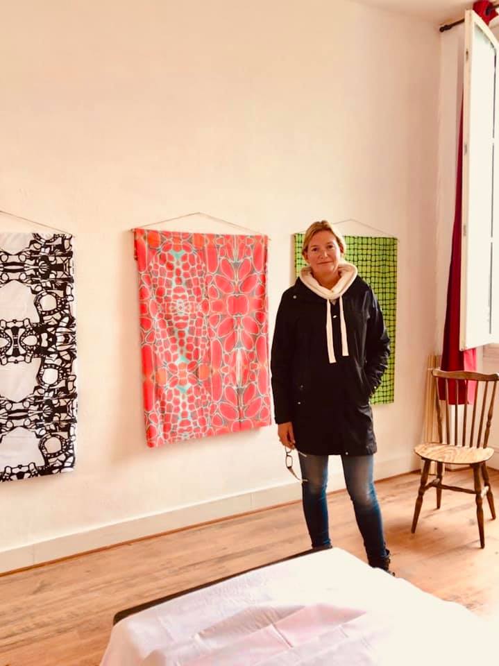 A woman in a black coat is standing in a room with paintings on the wall.