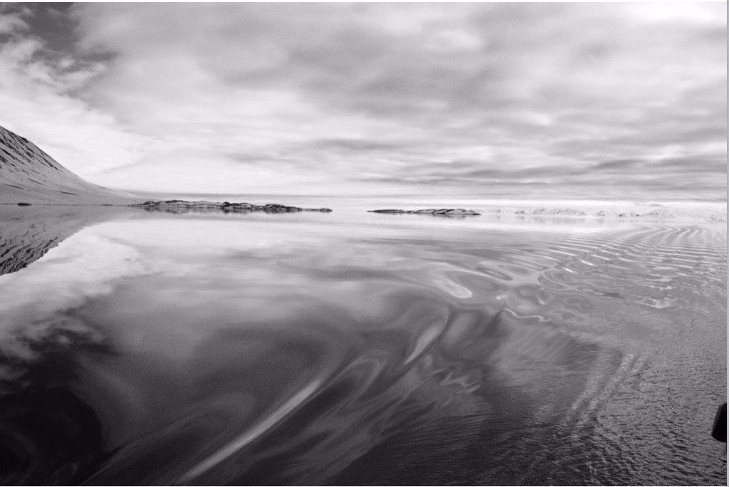 A black and white photo of a body of water with a mountain in the background.