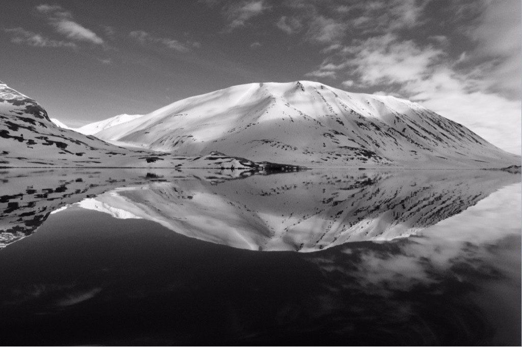 A black and white photo of a mountain reflected in a lake