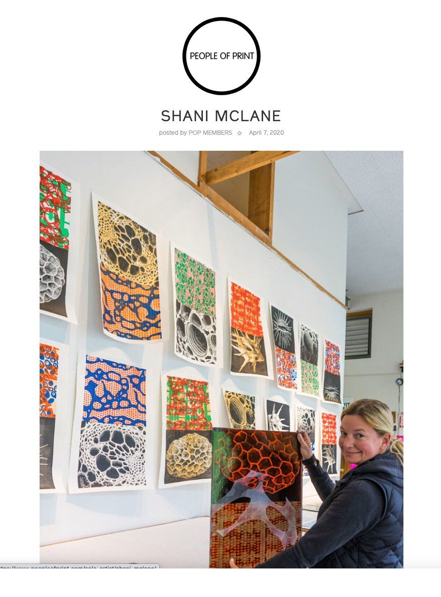 A woman is holding a painting in front of a wall of paintings by shani mclane