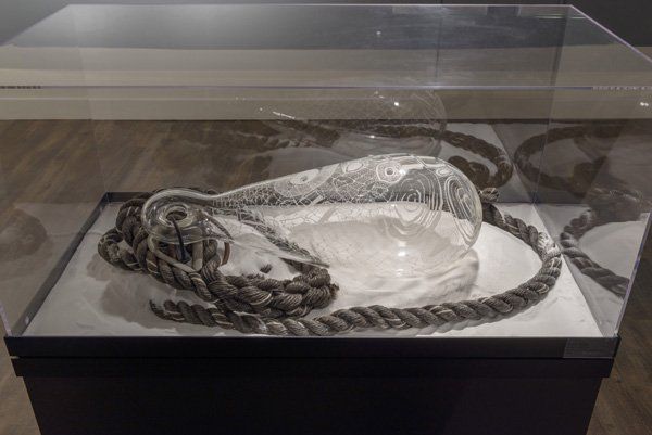 A glass container with a rope around it is in a glass case.