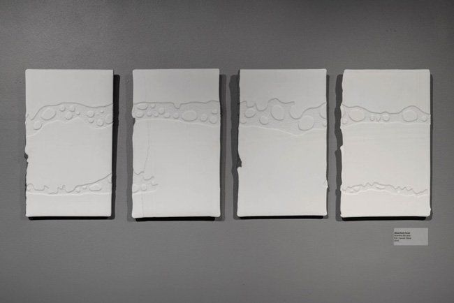 Four white paintings are sitting on a gray wall.