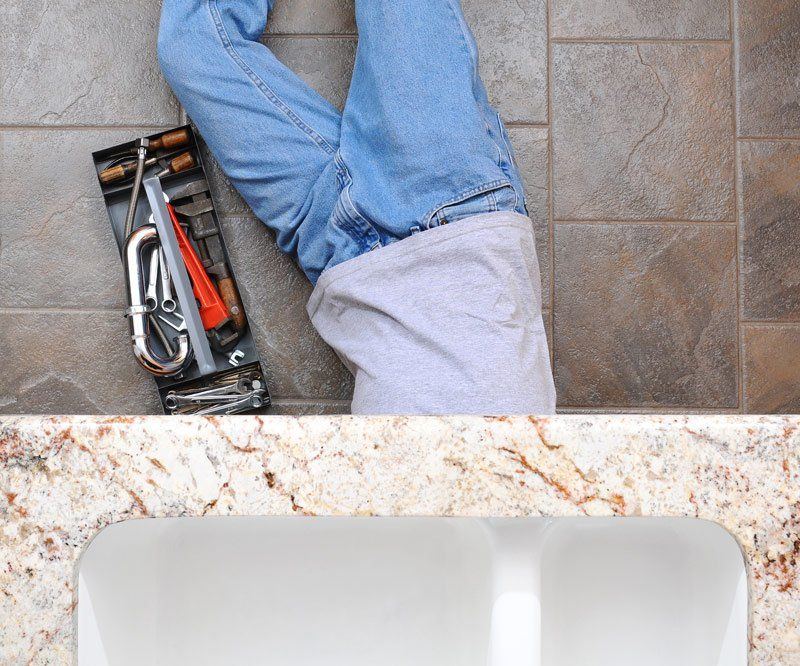 Plumber Laying Under A Kitchen Sink — Dempsey Plumbing in Long Jetty