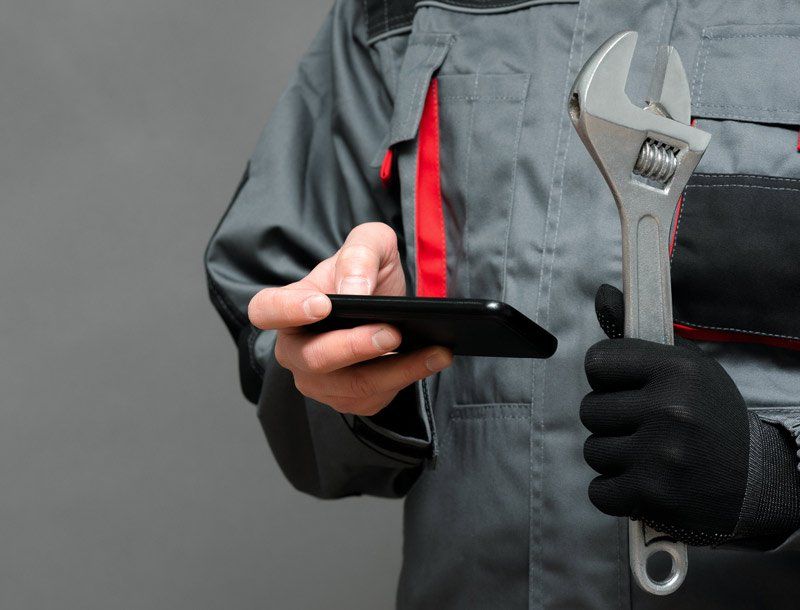 Plumber With A Mobile Phone And Wrench — Dempsey Plumbing in Wyong