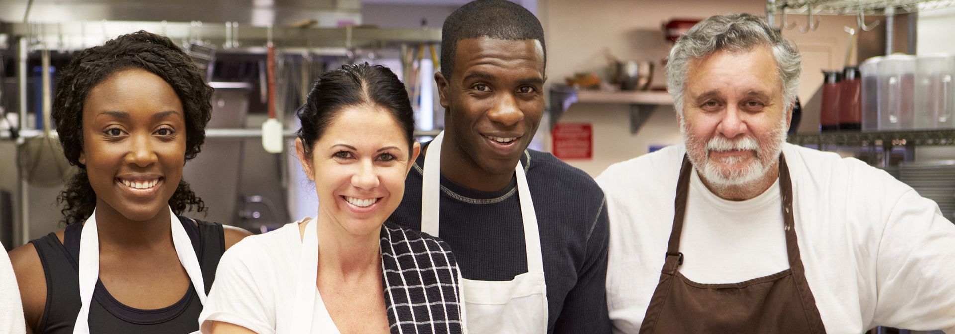 A group of people wearing aprons are posing for a picture in a kitchen.