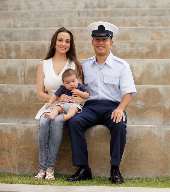 A man in a uniform sits on a set of stairs with a woman holding a baby.