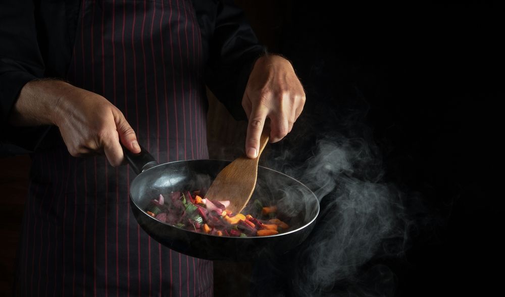 A person is cooking food in a frying pan with a wooden spatula.