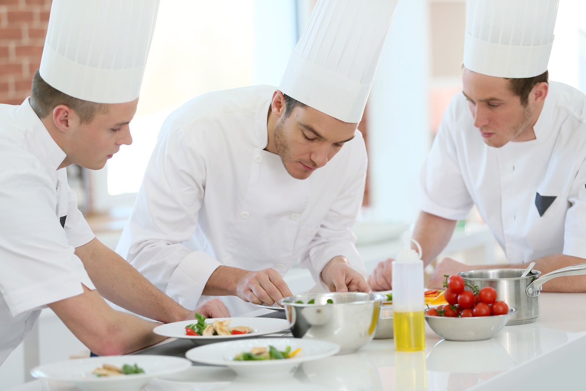 Three chefs are preparing food in a kitchen.