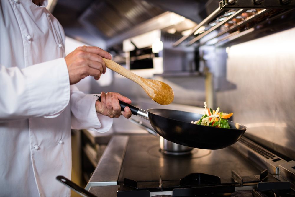 A chef is stirring vegetables in a wok with a wooden spoon.