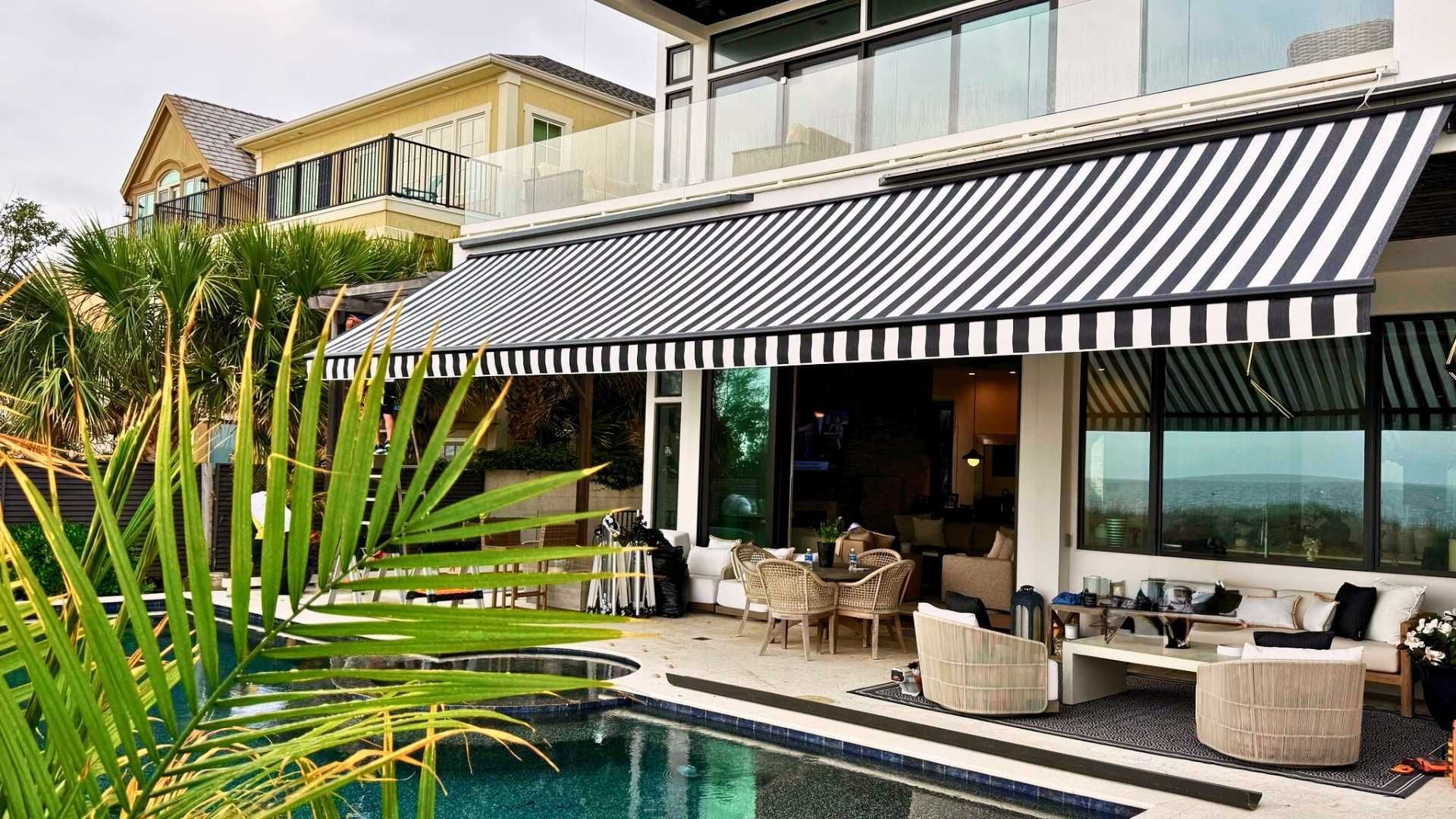 House with a black and white striped awning over a patio with pool, seating, and dining.