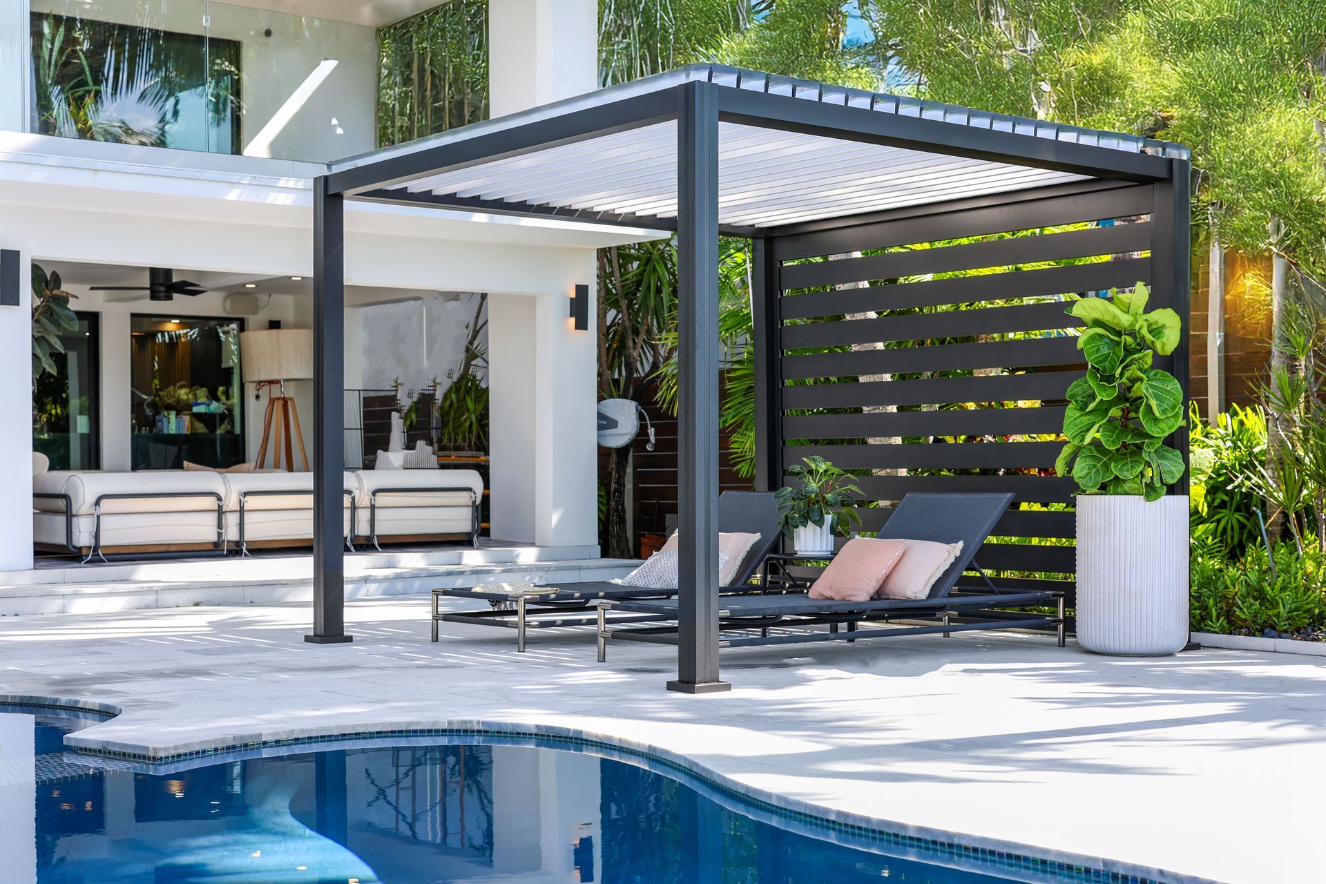 Poolside pergola with lounge chairs and decorative privacy wall.