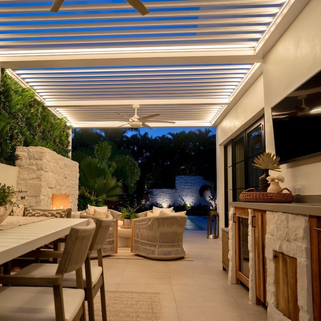 Outdoor patio with dining table, fireplace, bar, seating, and pergola with warm lighting.