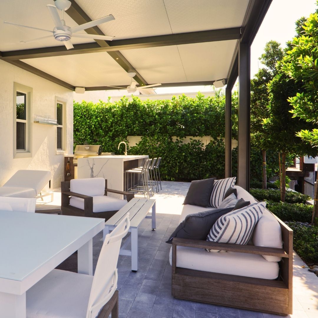 Outdoor patio with white furniture, a kitchen, and a hedge.