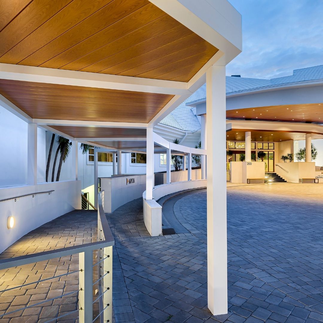 White pillars support a curved, covered walkway with a brick patio in front of a building.