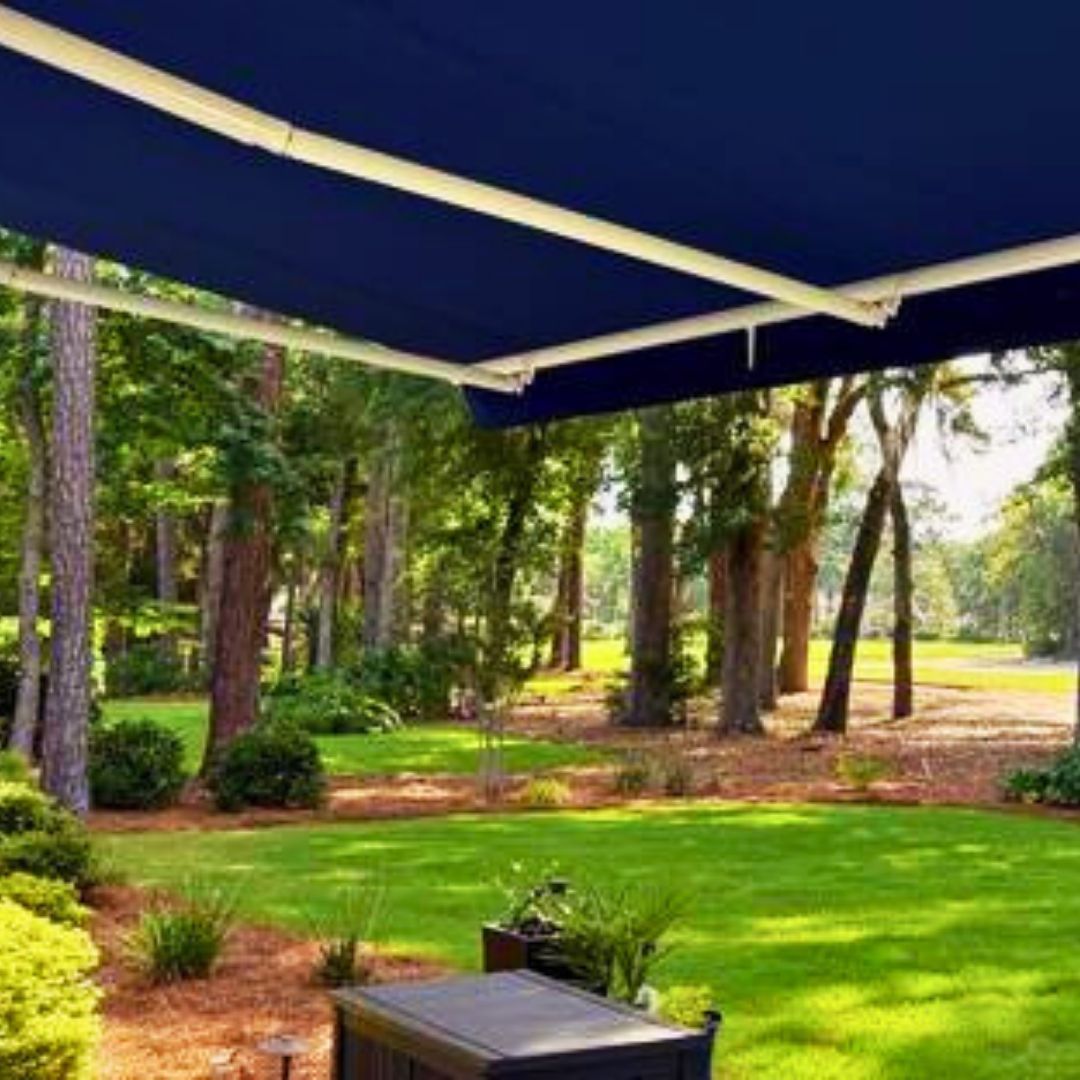 Dark blue awning over a backyard with green grass, trees, and a table.