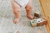 Baby standing on a patterned rug, wooden blocks nearby.