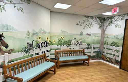 Waiting room with farm scene mural, wooden benches, and exit sign.