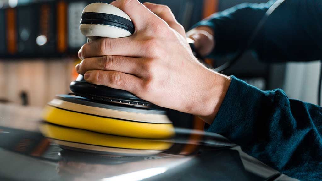 Person using a rotating yellow buffer on a reflective metallic surface, indoors.
