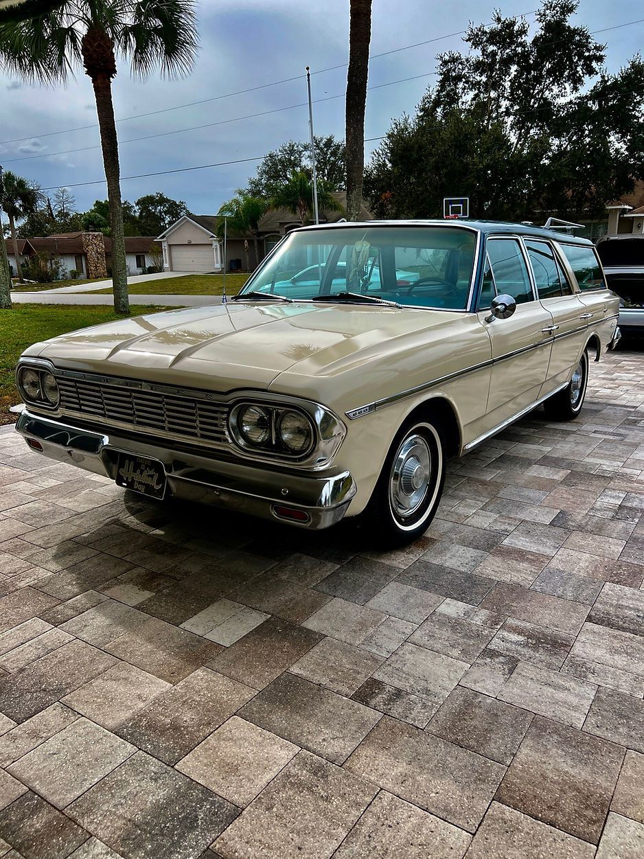 White vintage station wagon parked on a brick driveway, suburban setting.