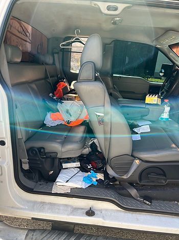 Interior of a dirty truck; clothes, papers, and other items strewn about the seats and floor.