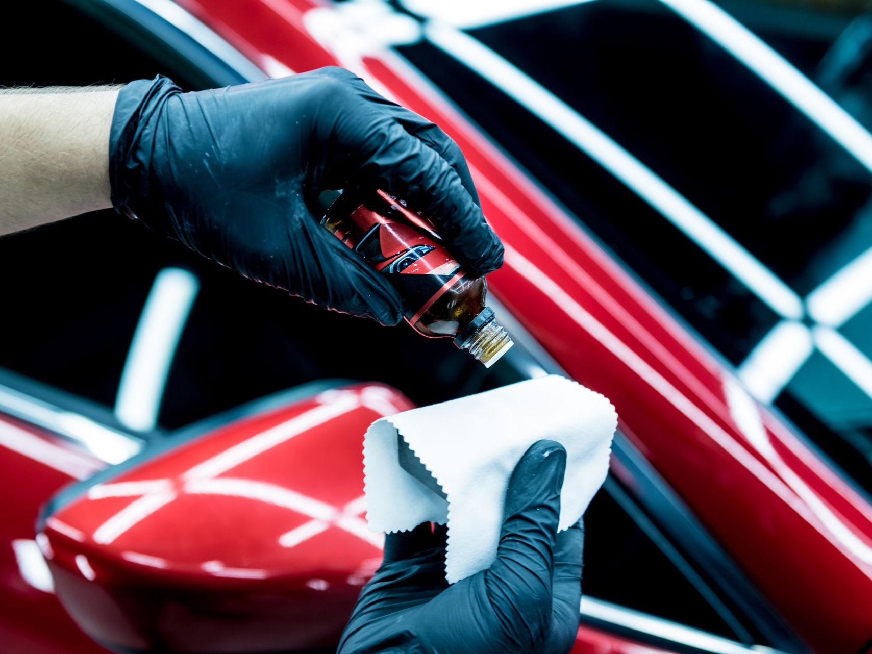 Person in black gloves applying ceramic coating to a car's surface with a microfiber cloth.