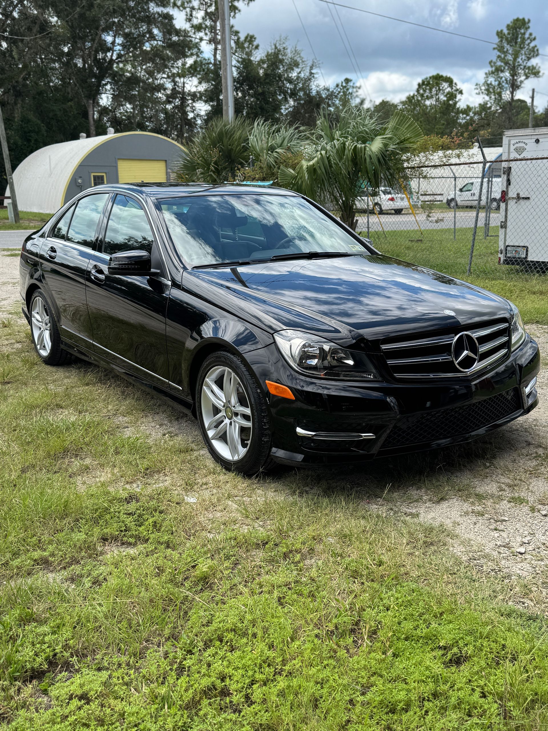 Black Mercedes-Benz sedan parked on grass. Building and trees in the background. Sunny day.