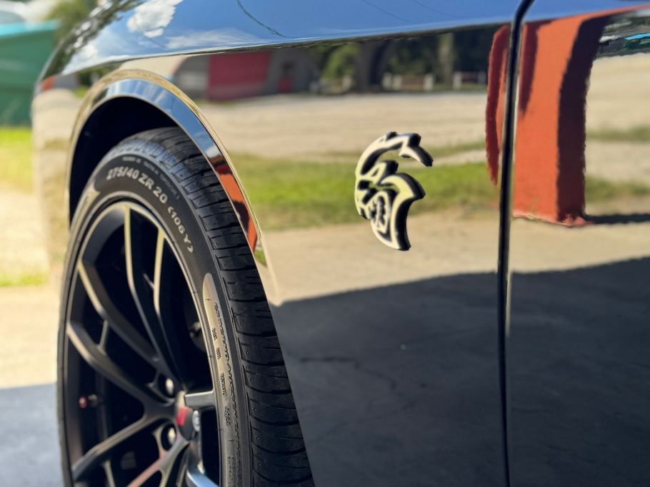 Black Dodge Challenger Hellcat with a wheel and emblem visible.