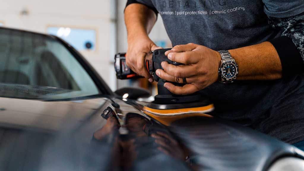 Person polishing a car with an electric buffer in a garage.