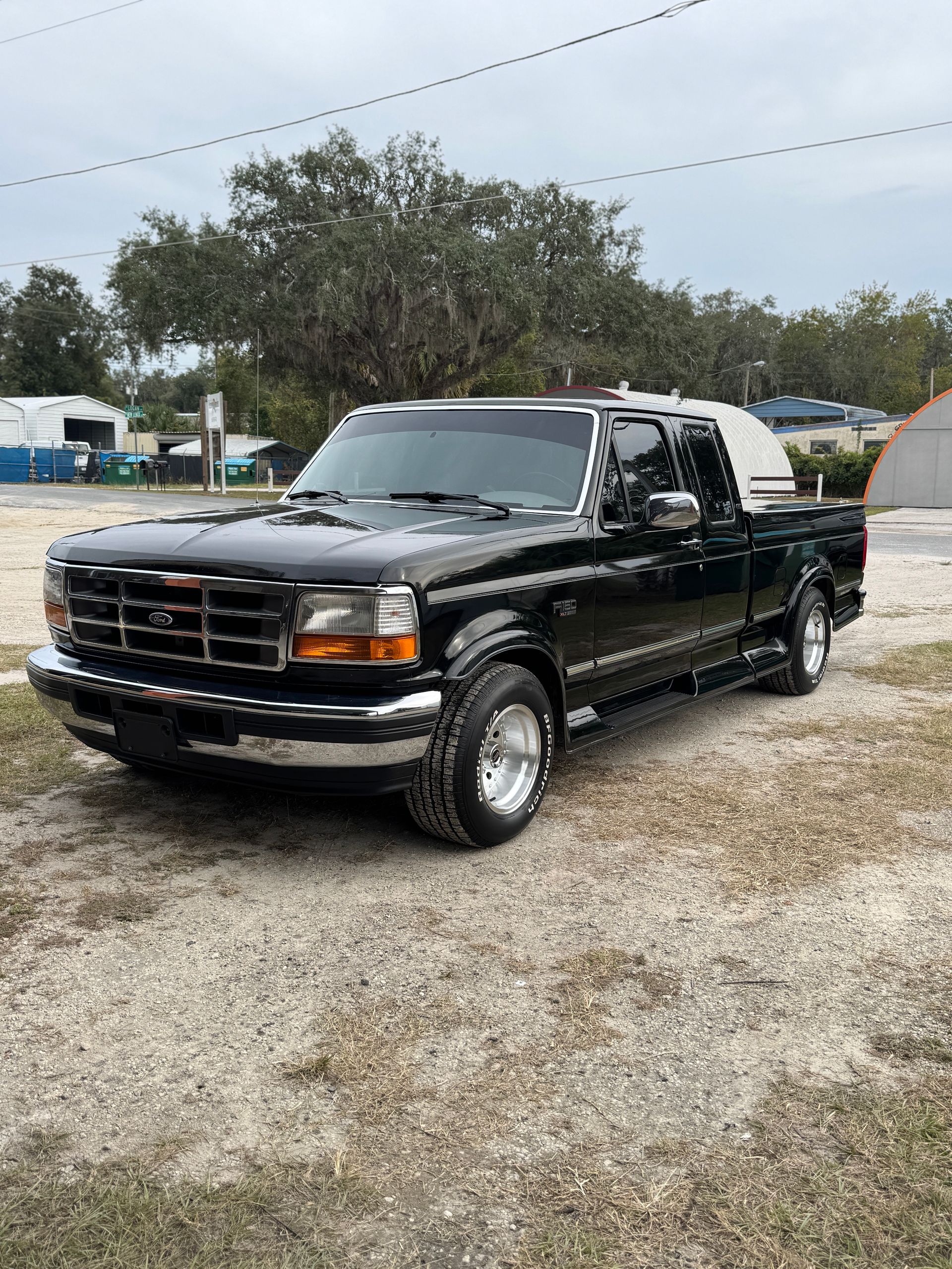 Black Ford F-150 pickup truck with white camper shell parked on gravel under an overcast sky.