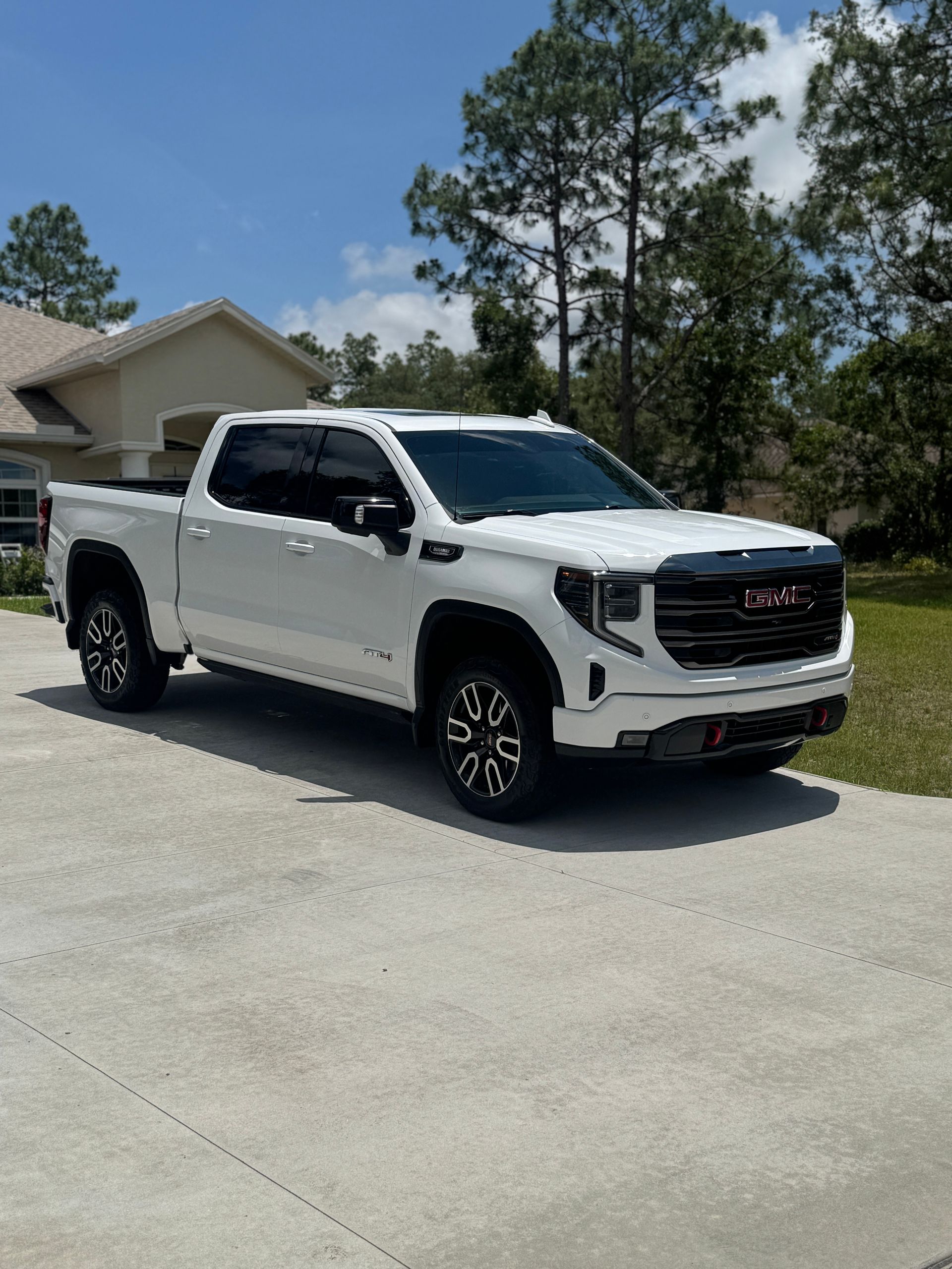 White GMC Sierra truck parked on a concrete driveway in front of a house.