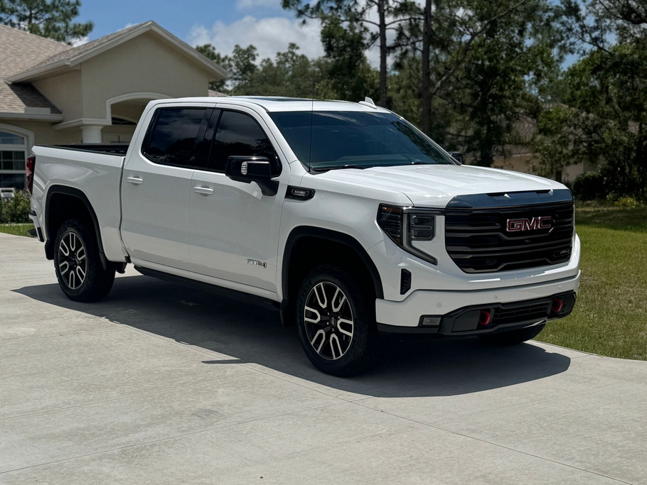 White GMC Sierra truck parked in front of a house on a sunny day.