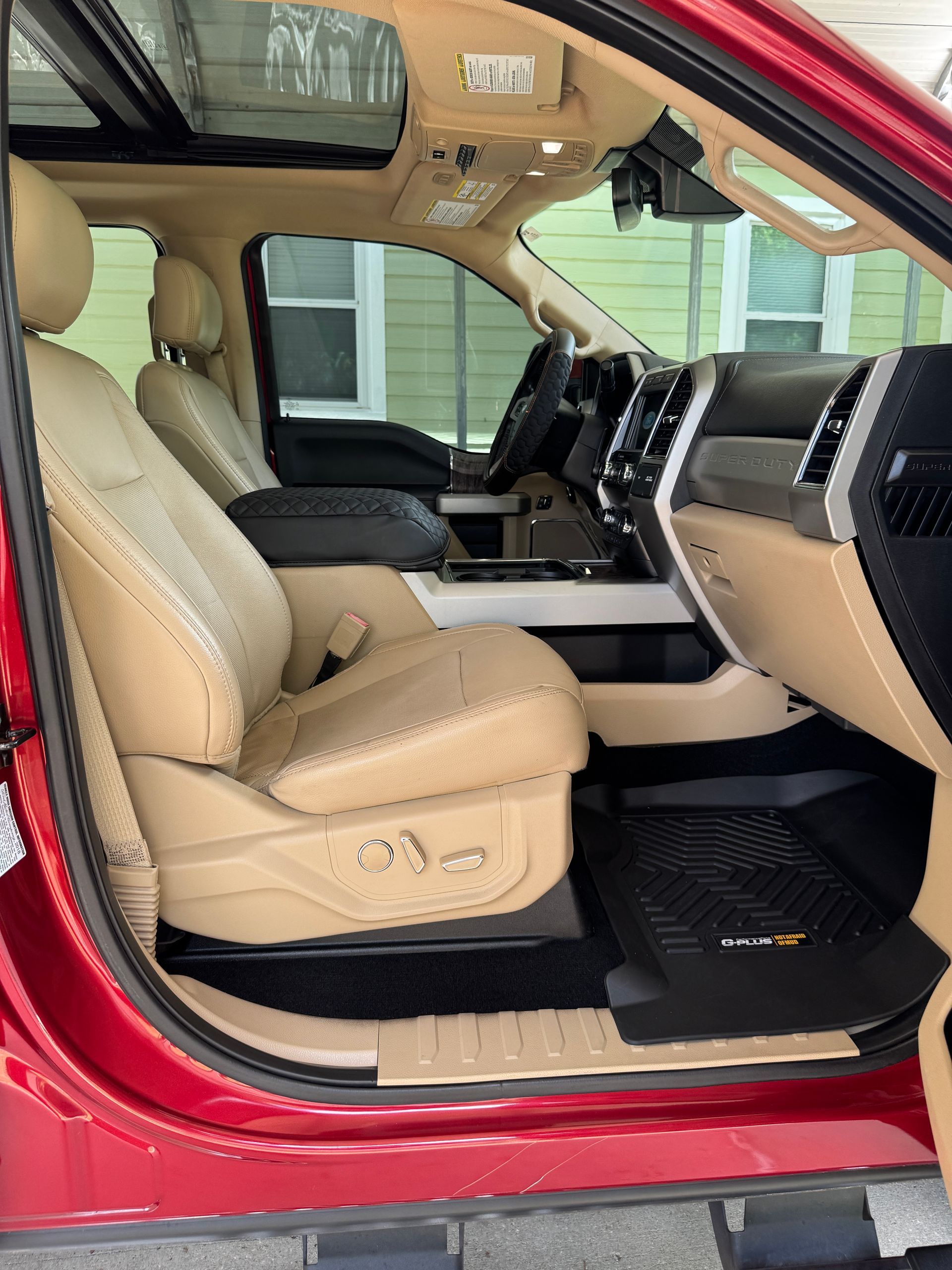 Tan interior of a red truck with a black floor mat, open sunroof, and leather seats.