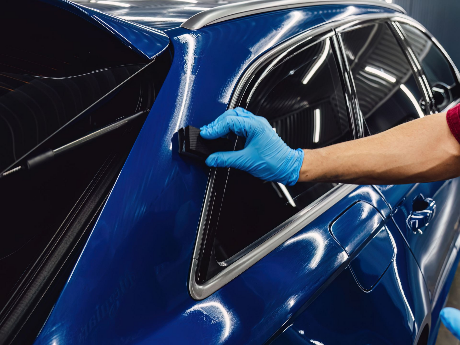 Person in blue gloves applying ceramic coating to a shiny blue car.
