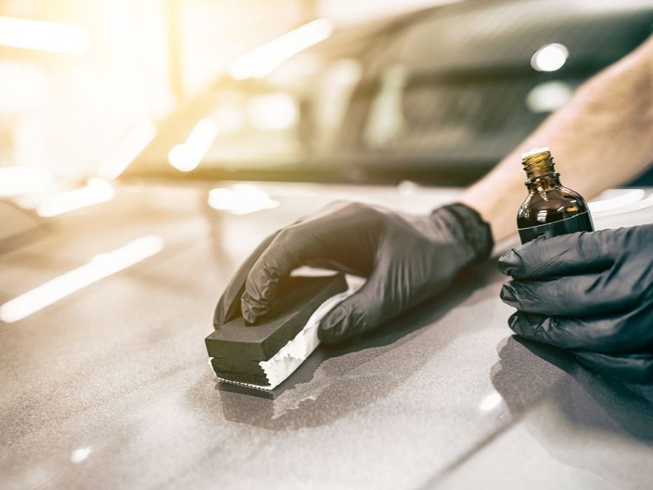 Person wearing black gloves applying ceramic coating to a car's hood.