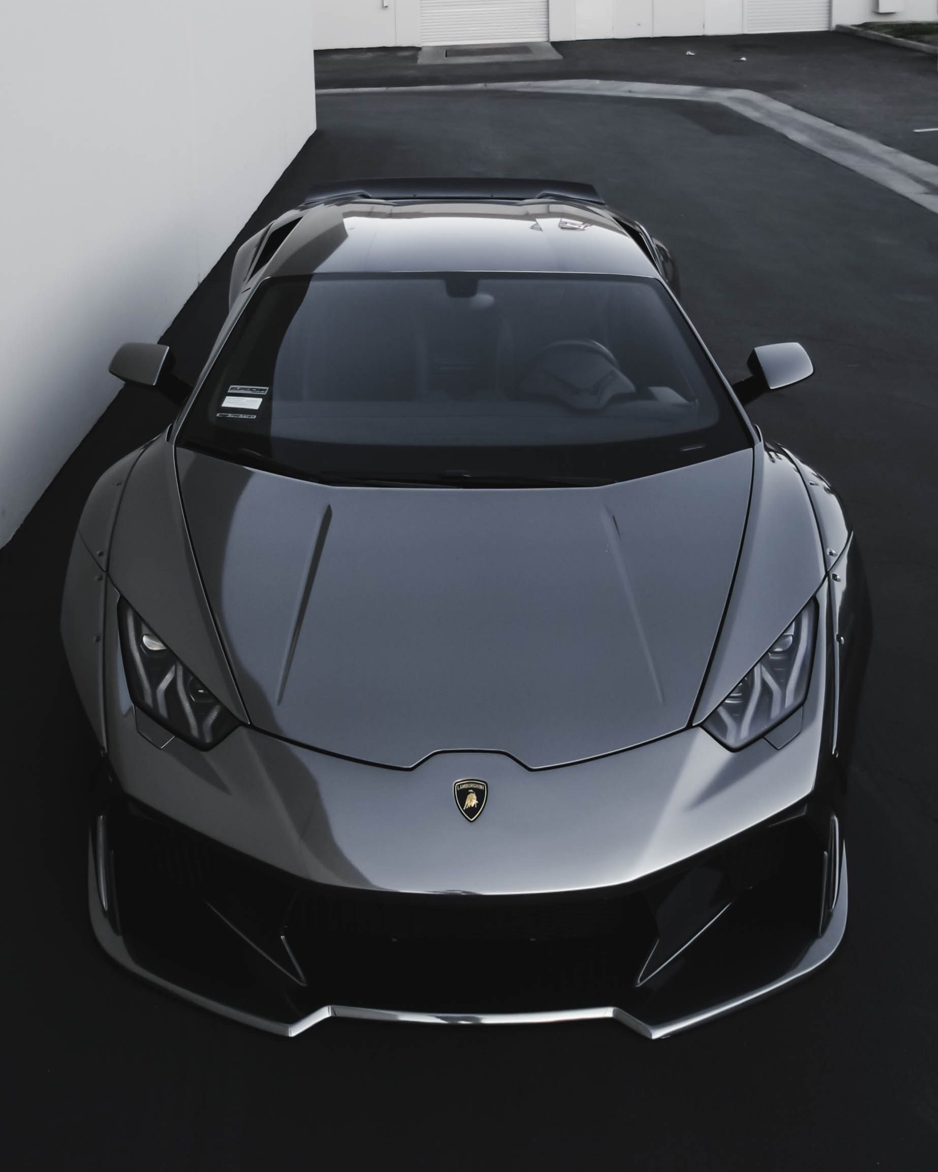 Gray Lamborghini sports car parked next to a white wall.