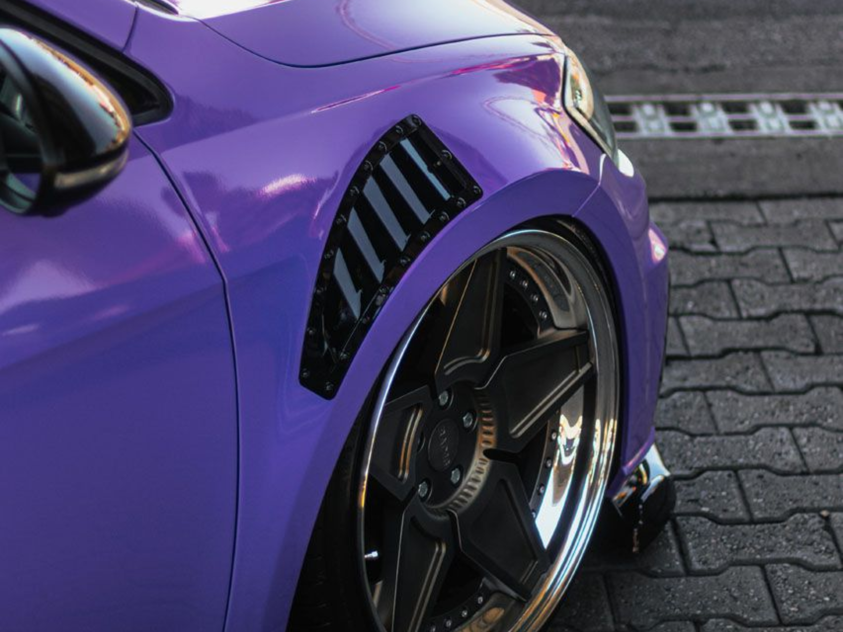 Purple car fender with black vents and a shiny black wheel.