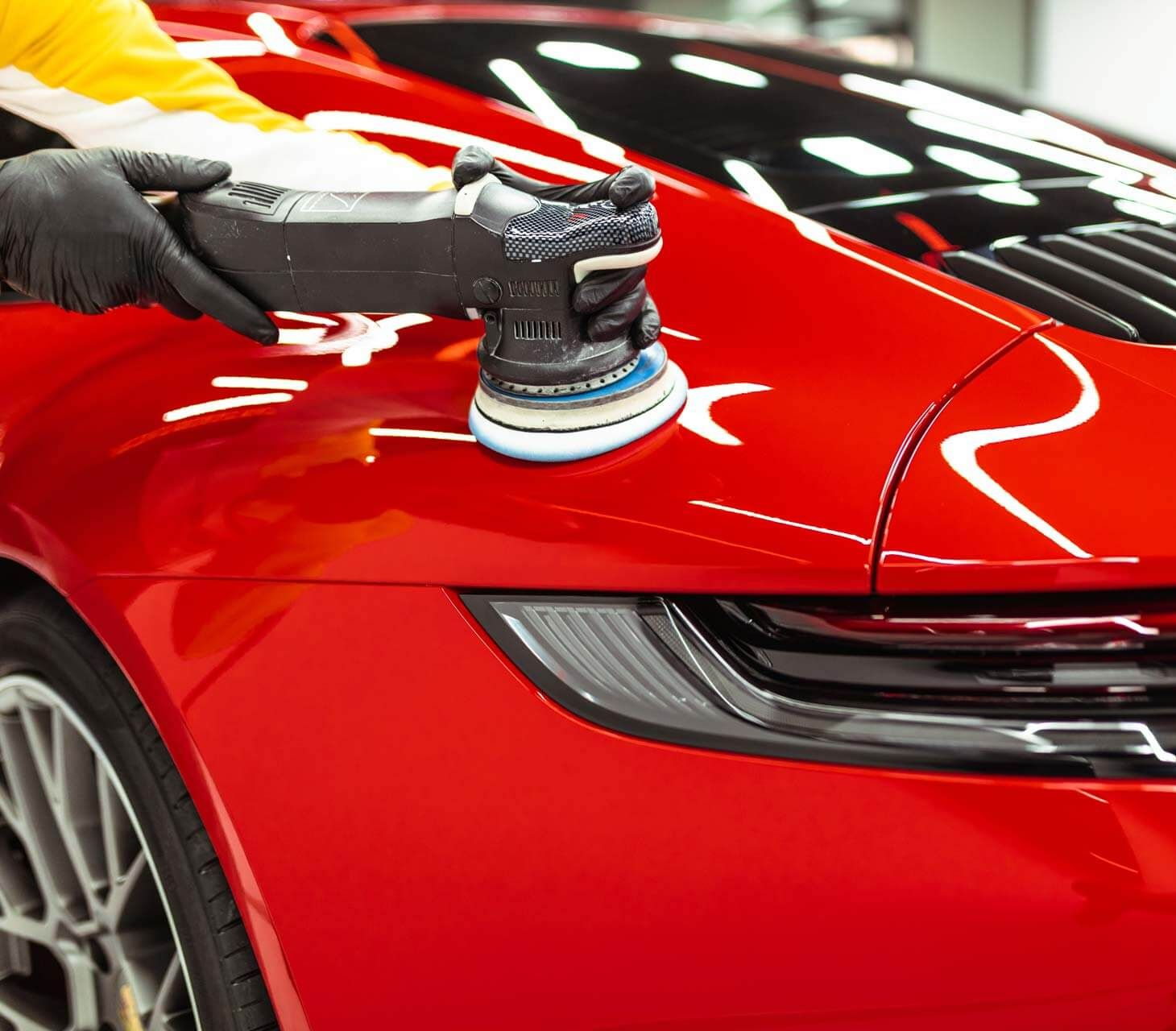 Person using a polishing machine on a red car. The car is being detailed.
