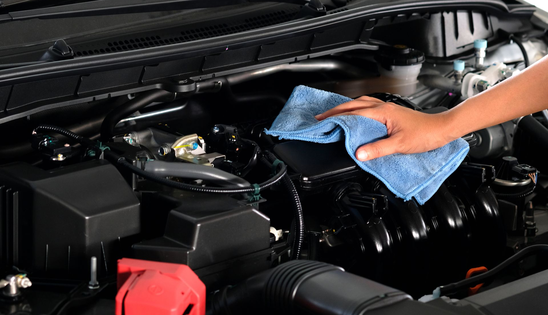 Person's hand with blue cloth wiping a clean car engine bay.
