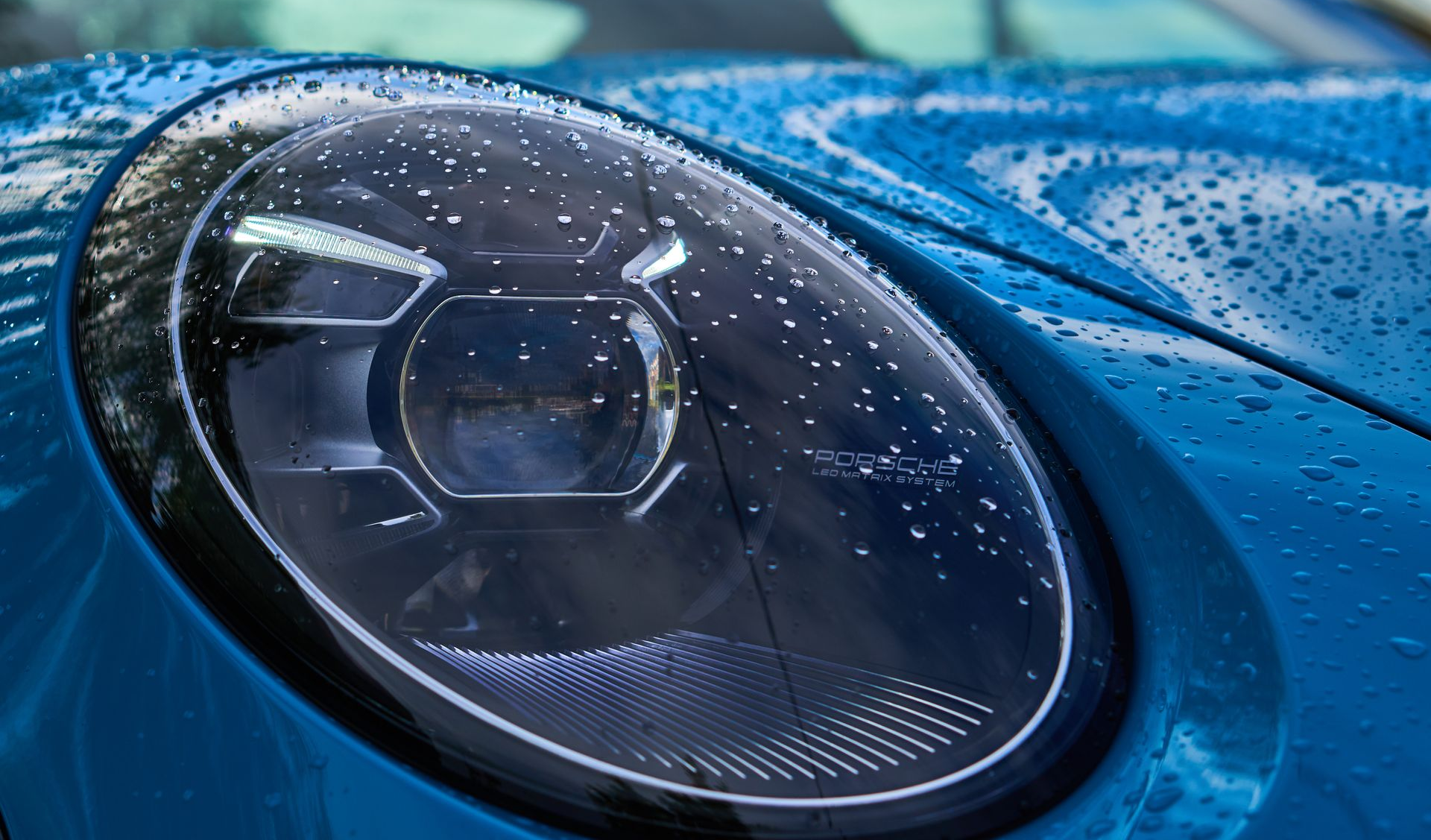 Blue Porsche headlight close-up with water droplets.